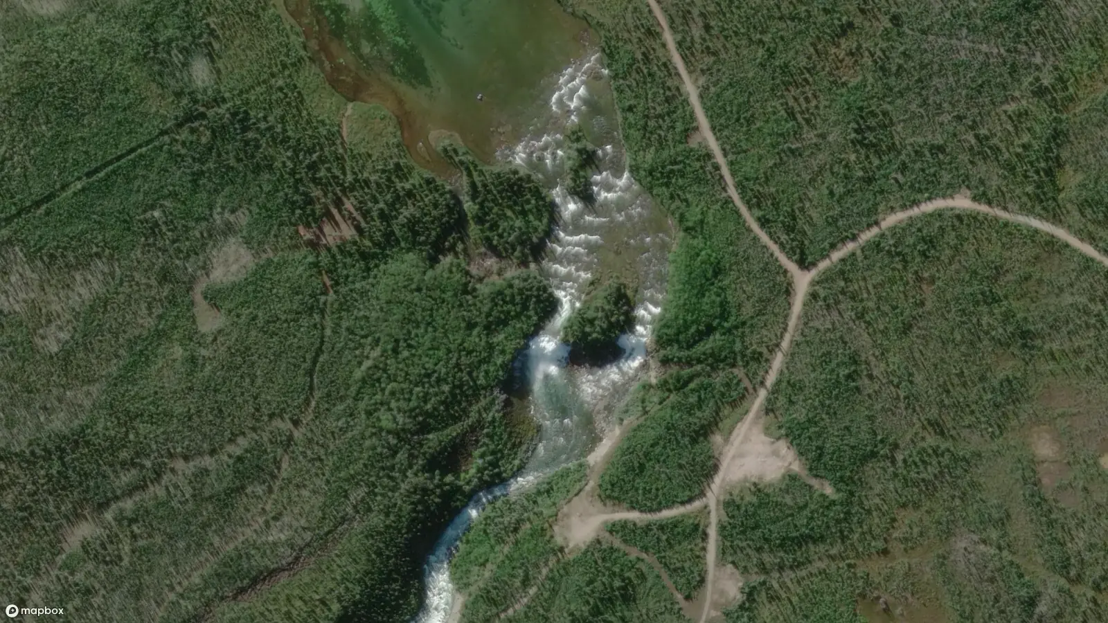 The wide Lac La Martre river narrows and plunges over a steep drop, with white rapids visible from the air. A utility road is visible on the right shore of the river, and portage footpaths are visible on the left shore of the river.