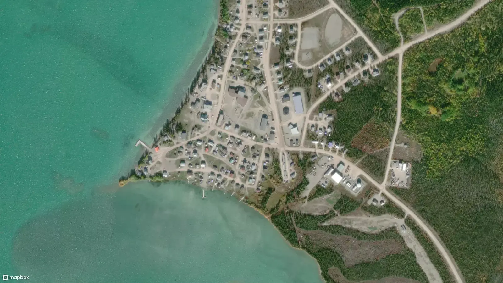 Satellite view of the community of Whatì on the shores of Lac La Martre. The jade green Lac La Martre is visible on the left, with the town built up around a natural point that edges out into the water.